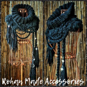 May include: A black chunky knit infinity scarf featuring a thick ribbed collar, layered braided cords, and dangling fringe. The scarf is adorned with silver-toned star and crescent moon charms. The text Rohan Made Accessories is visible.