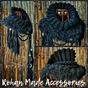 May include: A black chunky knit cowl scarf featuring a ribbed collar, textured fringe, and braided elements. The scarf is adorned with silver-toned star and crescent moon charms hanging from long fabric strips, creating a layered appearance.