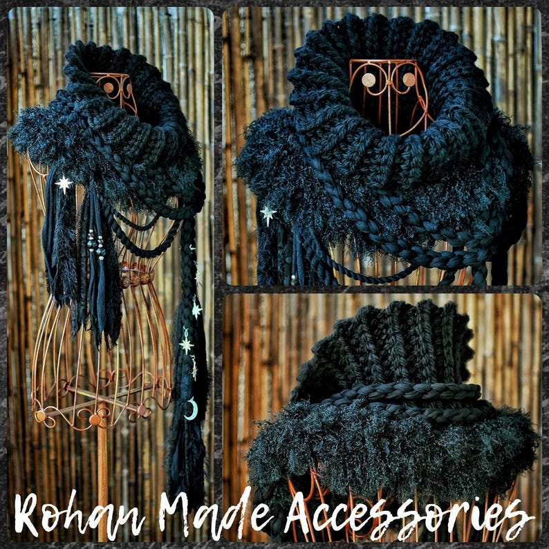 May include: A black chunky knit cowl scarf featuring a ribbed collar, textured fringe, and braided elements. The scarf is adorned with silver-toned star and crescent moon charms hanging from long fabric strips, creating a layered appearance.