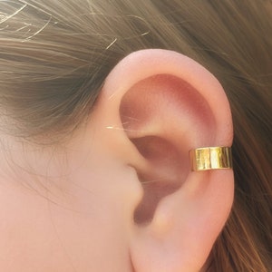 May include: A gold ear cuff, worn on the upper part of the ear, is a simple and elegant piece of jewelry.