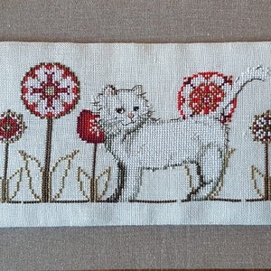 May include: White cat with red flowers and green leaves embroidered on a white linen background.