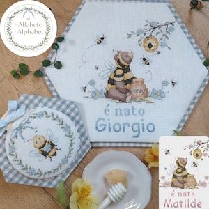 Può includere: Articoli per bambini a punto croce con tema api e miele. Il pezzo principale presenta un orso vestito da ape, con la scritta "é nato Giorgio". È incluso anche un pezzo rotondo più piccolo con un disegno di ape e un pezzo esagonale.