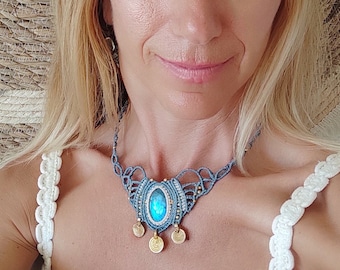 May include: A woman wearing a white crocheted top with a blue and gold macrame necklace featuring a large oval gemstone pendant.