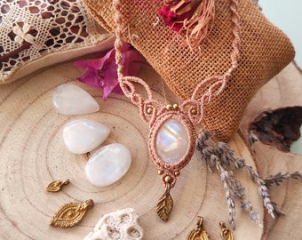 Puede incluir: Un collar de macramé con un gran colgante de piedra lunar iridiscente y detalles en latón. El collar se muestra sobre una superficie de madera con otras piedras lunares y abalorios de latón.