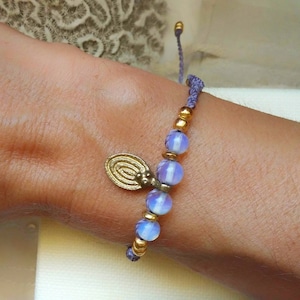 Puede incluir: Un brazalete morado y dorado con un dije y cuentas de color ópalo.