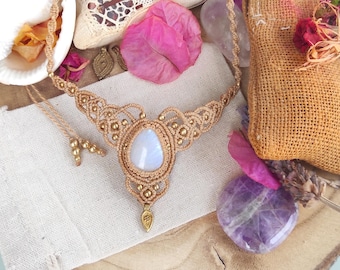 Puede incluir: Un delicado collar de macramé con un colgante de piedra lunar en forma de lágrima. El collar está hecho con cordón beige natural y cuentas doradas.