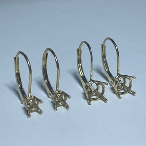 May include: Four gold earring settings with a lever back closure. The settings are different sizes.