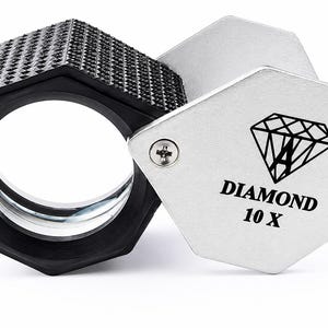 May include: A jeweler's loupe with a black, textured, hexagonal outer casing and a silver-colored metal cover. The cover features a black graphic of a diamond and the text "DIAMOND 10 X" with two visible screws securing the metal plate to the frame.