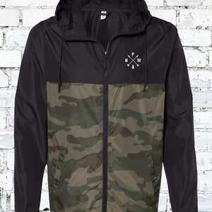 May include: A black and camouflage windbreaker jacket with a zipper closure and a hood. The jacket has a small embroidered logo on the chest that says "N W P" with an arrow pointing down.