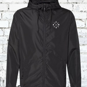 May include: A black hooded windbreaker jacket with a zipper closure and a white embroidered compass design on the left chest. The compass design features a tree and the letters "N", "P", "W" and "E".