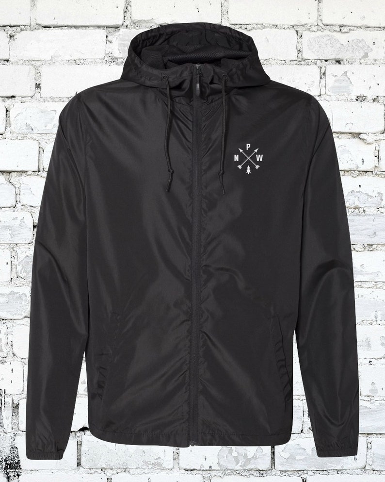 May include: A black hooded windbreaker jacket with a zipper closure and a white embroidered compass design on the left chest. The compass design features a tree and the letters "N", "P", "W" and "E".