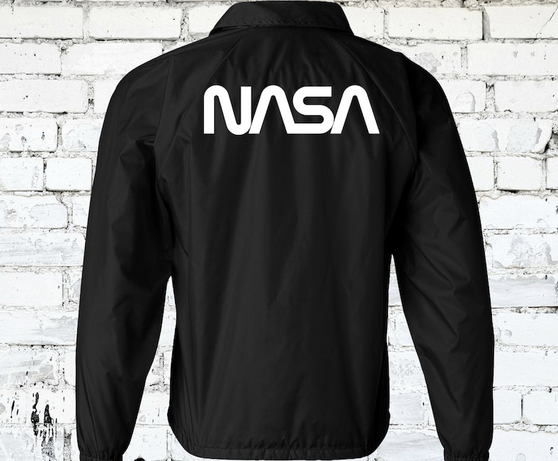 Puede incluir: Chaqueta cortavientos negra con un logotipo blanco de la NASA en la espalda.