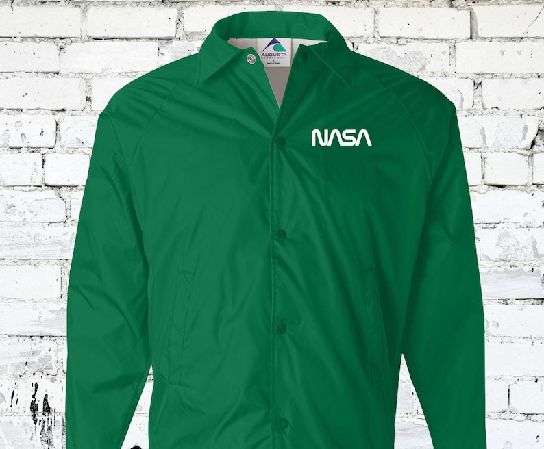 Puede incluir: Una chaqueta verde con botones y un logotipo blanco de la NASA en el pecho izquierdo.