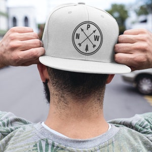 May include: A white baseball cap with a black compass design featuring the letters "N", "W", "P", and "W" inside a circle. The compass design also includes a small pine tree.