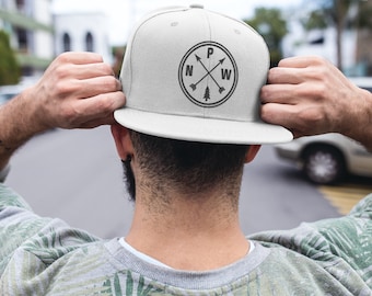 May include: A white baseball cap with a black compass design featuring the letters "N", "W", "P", and "W" inside a circle. The compass design also includes a small pine tree.