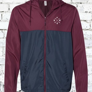 May include: A maroon and navy blue windbreaker jacket with a zipper closure and a hood. The jacket has a small embroidered logo on the chest that says "PNW" with arrows pointing north, west, and south.