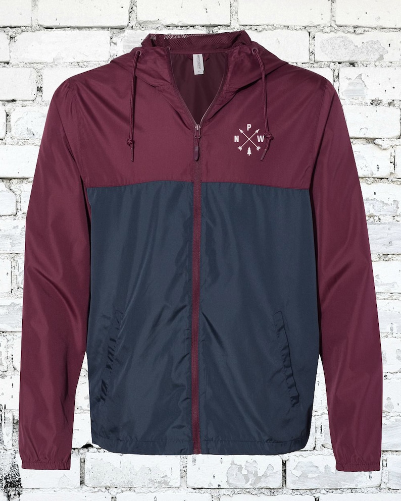 May include: A maroon and navy blue windbreaker jacket with a zipper closure and a hood. The jacket has a small embroidered logo on the chest that says "PNW" with arrows pointing north, west, and south.
