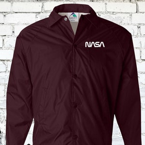 Puede incluir: Una chaqueta de b&eacute;isbol granate con un logotipo de la NASA blanco en el pecho izquierdo.