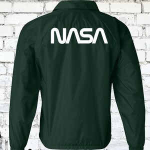 Puede incluir: Una chaqueta verde oscuro con un logotipo blanco de la NASA en la espalda.