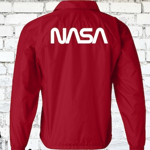 Puede incluir: Chaqueta cortavientos roja con un logotipo blanco de la NASA en la espalda.