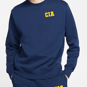 May include: A navy blue sweatshirt with a yellow "CIA" logo on the chest.