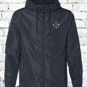 May include: A dark blue hooded jacket with a zipper closure and a white embroidered compass design on the chest. The compass design features the letters N, W, and P with a small tree in the center.