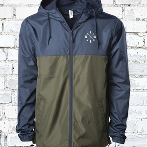 May include: A navy blue and olive green hooded jacket with a zipper closure. The jacket has a white logo on the chest that says "P NW" with arrows pointing north, west, east, and south.