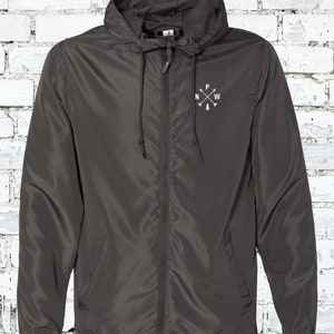 May include: A dark gray hooded jacket with a zipper closure. The jacket has a small embroidered compass design on the left chest with the letters "N", "W", "P", and "E" around a small pine tree.