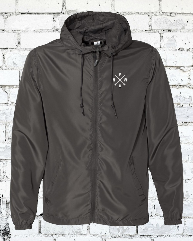 May include: A dark gray hooded jacket with a zipper closure. The jacket has a small embroidered compass design on the left chest with the letters "N", "W", "P", and "E" around a small pine tree.