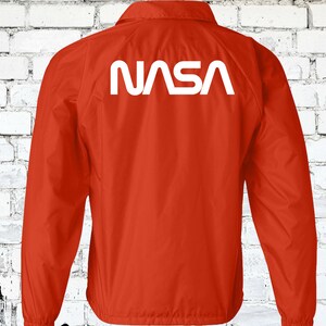 Puede incluir: Chaqueta de nylon roja con un logotipo blanco de la NASA en la espalda.