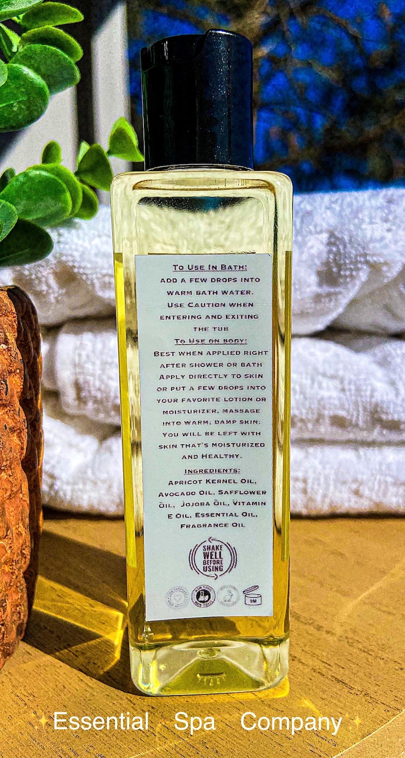 May include: A clear glass bottle of Essential Spa Company oil with a black cap. The label provides instructions for use in the bath and on the body, and lists ingredients like apricot kernel oil and vitamin E oil.