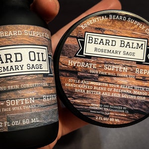 May include: A black bottle of beard oil and a round container of beard balm. Both products feature a wood-grain design and the text "Rosemary Sage." The beard oil is 2 fl oz / 60 ml. The balm is designed to hydrate, soften, and repair.