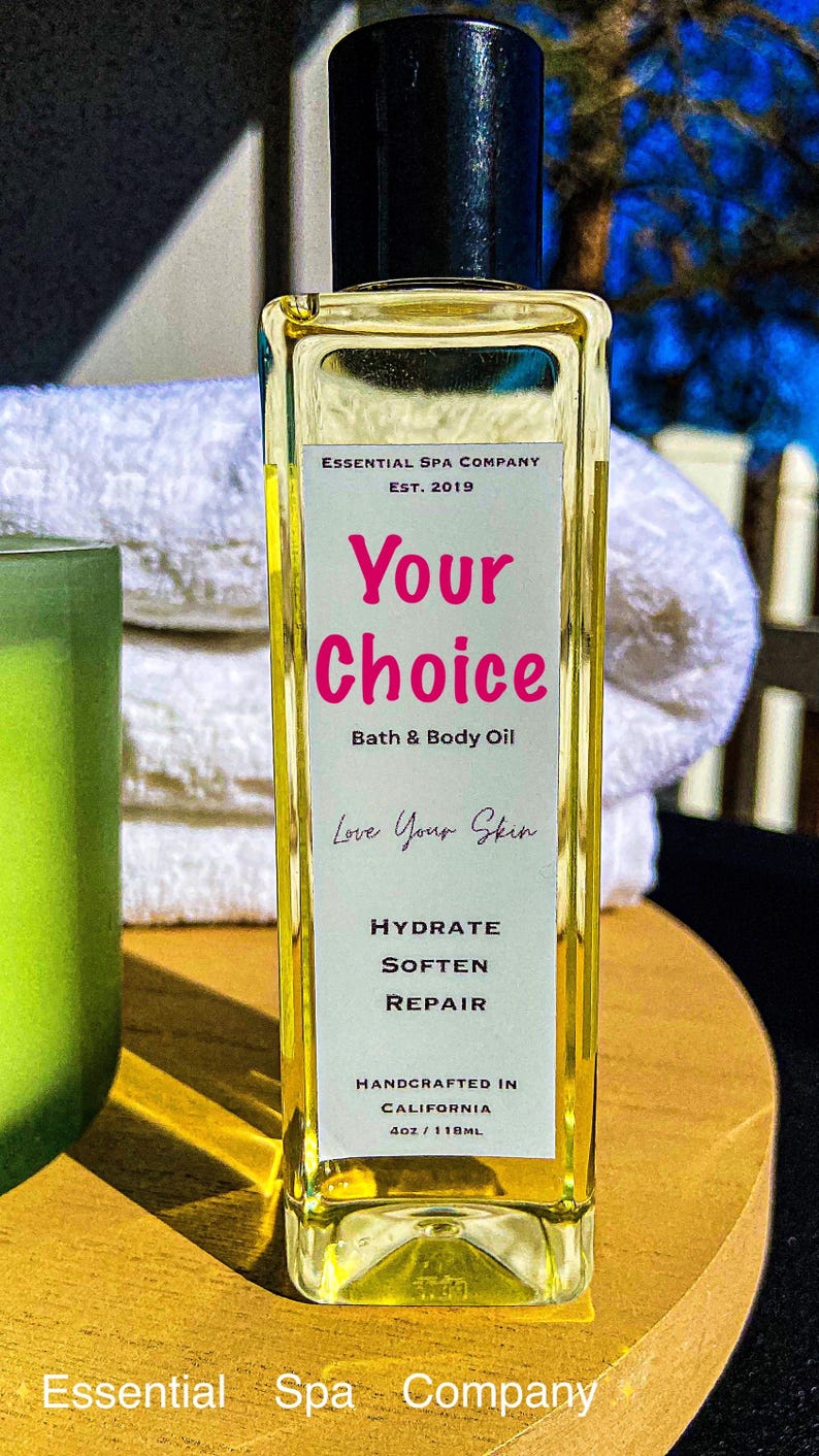 May include: A rectangular glass bottle of bath and body oil with a black cap. The label reads "Your Choice" in pink, with "Bath & Body Oil" below. The bottle is 4oz/118mL and says "Handcrafted in California."