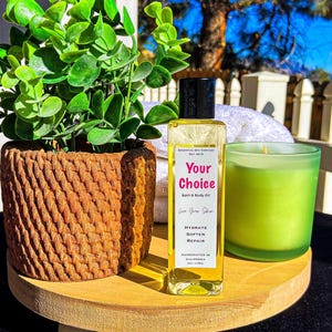 May include: A wooden tray holds a potted plant, a bottle of bath and body oil, and a green candle. The oil bottle has a black cap and a label that reads "Your Choice" and "Bath & Body Oil". The candle is in a green glass holder.