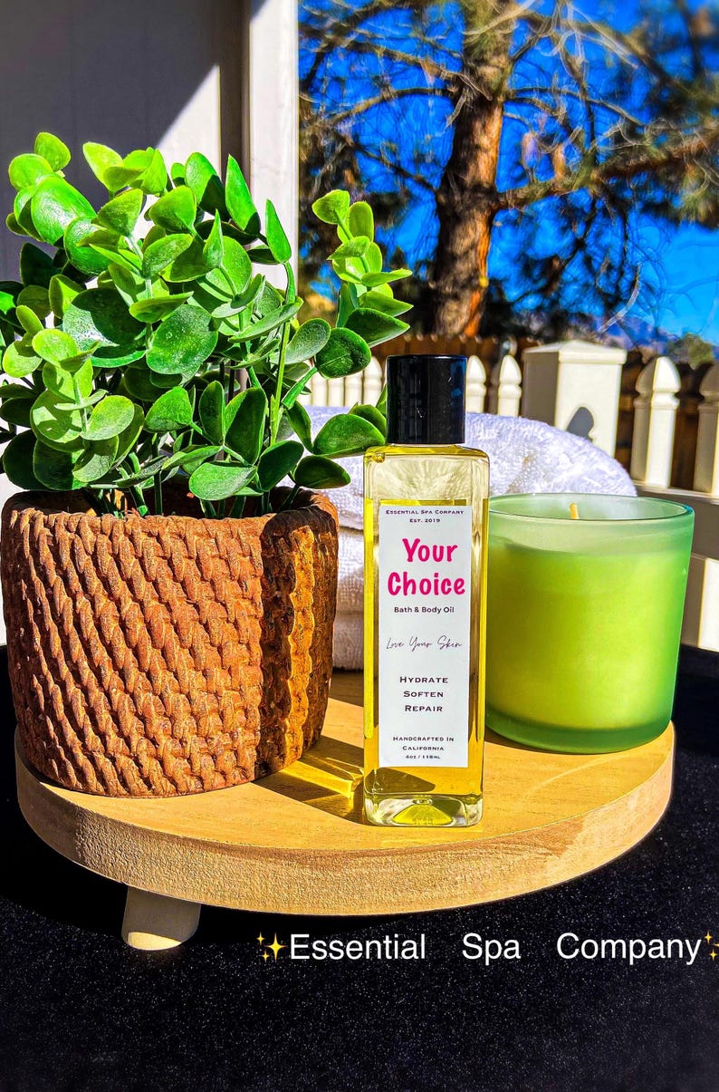 May include: A wooden tray holds a potted plant, a bottle of bath and body oil, and a green candle. The oil bottle has a black cap and a label that reads "Your Choice" and "Bath & Body Oil". The candle is in a green glass holder.
