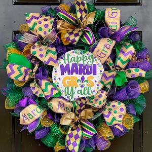 Op de afbeelding: Een feestelijke Mardi Gras-krans met groen, paars en goudkleurig gaas. De krans heeft decoratieve linten, strikken en een centraal bord met de tekst "Happy Mardi Gras Y'all". Het bord heeft een fleur-de-lis-symbool.