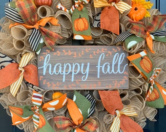 May include: A burlap wreath decorated with fall-themed ribbons, bows, and fabric pumpkins. The wreath has a wooden sign that reads "happy fall".