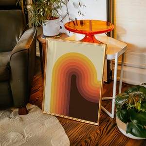 May include: A framed print with a retro-style design featuring a curved, multi-colored stripe pattern in shades of orange, yellow, brown, and red.