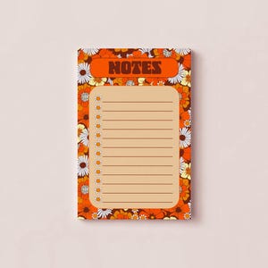 May include: A rectangular notepad featuring a vibrant orange and brown floral pattern with white daisies. The top section contains the word NOTES in bold brown letters. The center has a light tan area with horizontal lines and small daisy icons.