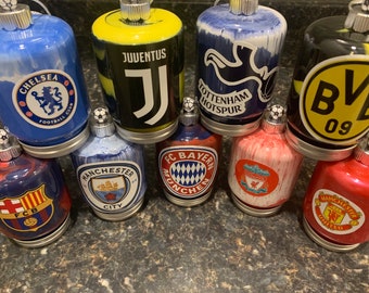 Op de afbeelding: Een verzameling kerstballen met voetbalthema's. Elke bal toont het logo van een team, waaronder Chelsea, Juventus, Tottenham Hotspur en Manchester United. De ballen hebben een zilveren dop en een kleine voetbal.