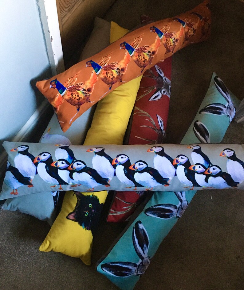 May include: A collection of colorful, decorative bolster pillows with various animal and nature-themed designs. The pillows feature images of puffins, a black cat, a pheasant, and a rabbit.