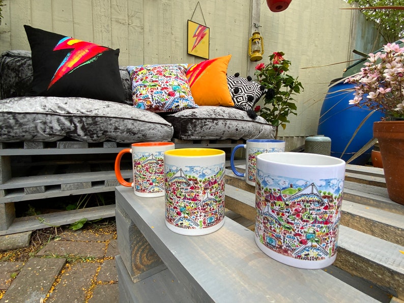 May include: Four ceramic mugs with colorful illustrations of a city skyline. The mugs are arranged on a wooden surface. The mugs are in different colors: orange, yellow, white, and blue.