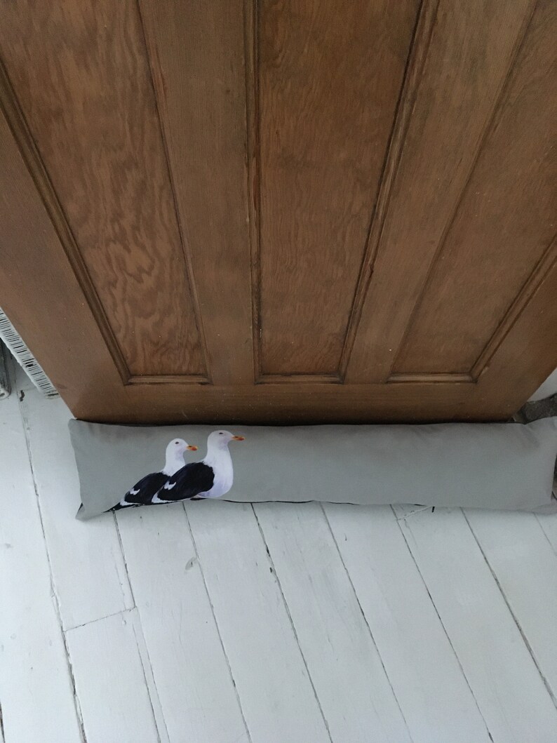 May include: A gray doorstop with a print of two seagulls. The doorstop is lying on a white wooden floor.