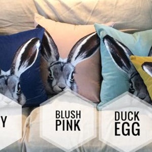 May include: Ten decorative throw pillows with a hare design in various colors, including burnt orange, navy, blush pink, duck egg, and orla gold. The pillows are arranged on a couch with a white background. The text "Mineral Blue" is visible in the top right corner of the image.