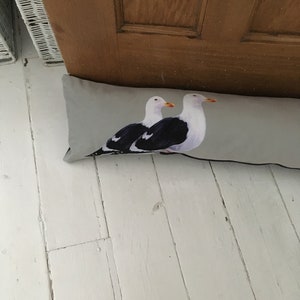 May include: A gray doorstop with a printed image of two seagulls. The seagulls are facing right and have black and white markings.