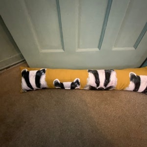 May include: A yellow doorstop with a repeating pattern of badger faces. The badger faces are black and white with pink noses.