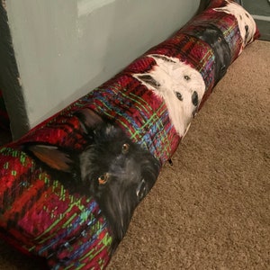 May include: A red, green and blue tartan doorstop with three dog faces printed on it. The dogs are a black terrier, a white terrier and a white terrier with black markings.
