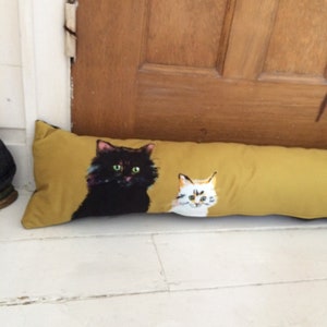 May include: A mustard yellow doorstop with a black cat and a white cat with orange markings printed on it.