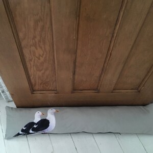 May include: A gray doorstop with a print of two seagulls. The doorstop is made of fabric and has a rectangular shape.