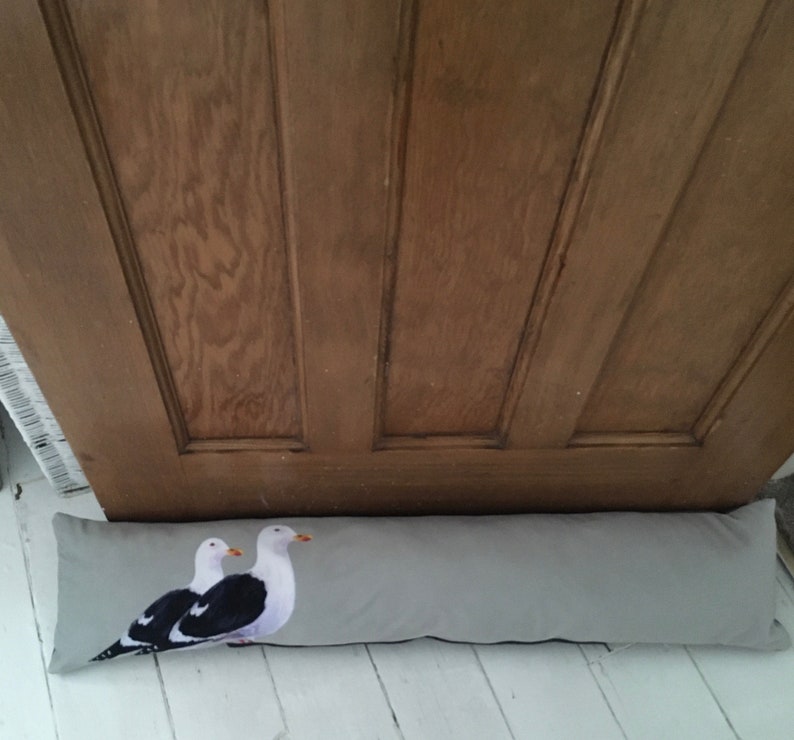 May include: A gray doorstop with a print of two seagulls. The doorstop is made of fabric and has a rectangular shape.